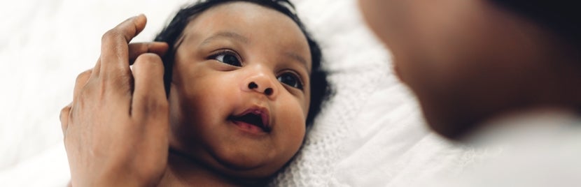 A newborn lying on a bed looking at their parent