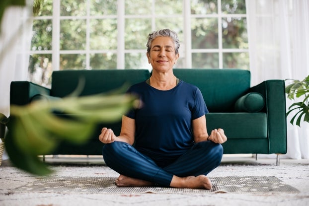 An older woman meditating in her own living room