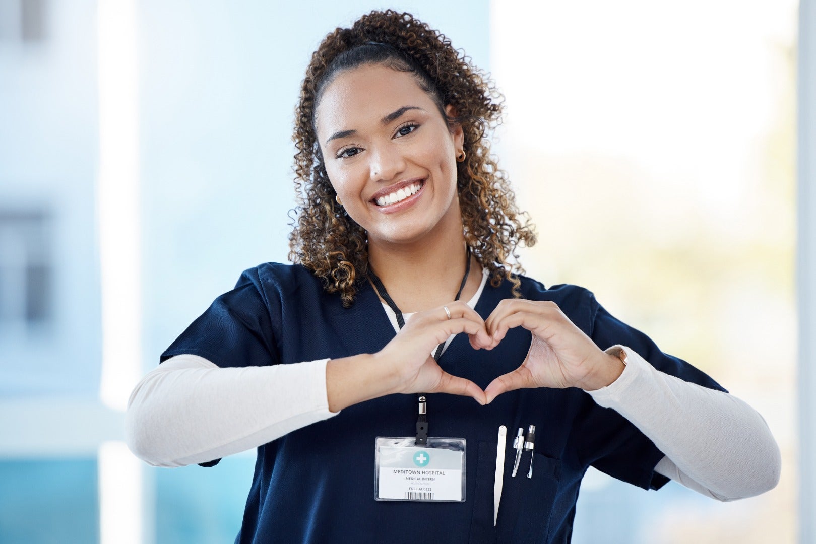 Woman in scrubs holding her hands in the shape of a heart